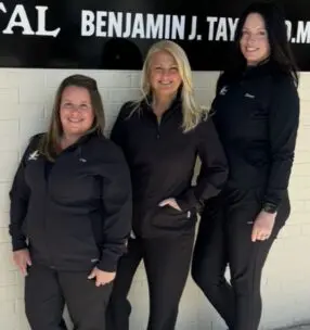 First Care Dental team members Lisa, Gwen, and Deven standing together in front of the Louisville office